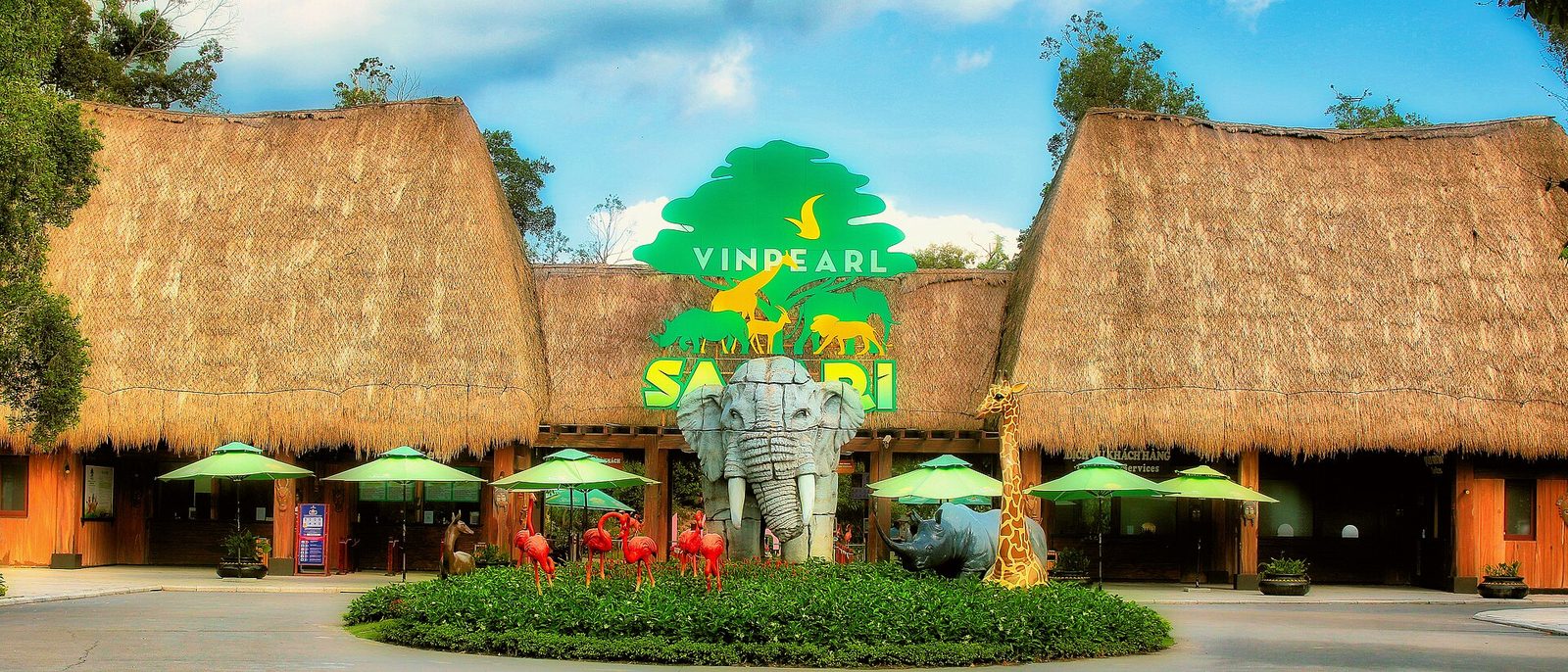 Giraffes and antelope in an open paddock at Vinpearl Safari Phu Quoc, with the park buildings behind